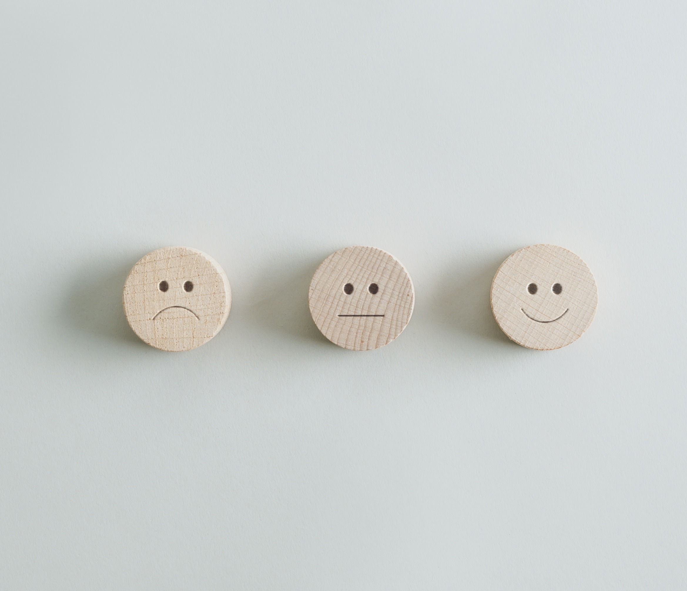 Wooden cut circles with faces representing positive, negative and neutral grade placed in a row over grey background. Wide view image with copy space.